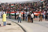 People sitting on stands holding Kurdish flags, and a big flag of Kurdistan