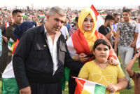 A man and woman wearing Kurdish clothing and a young girl holding a Kurdish flag