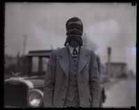 Stunt driver Hayward Thompson stands blindfolded with his Pontiac Six car behind him, Los Angeles, circa 1927