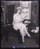 Actress Symona Boniface sitting on the edge of a table holding a newspaper, Los Angeles, circa 1924-1930