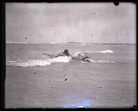 Surfer and Olympic swimmer Duke Kahanamoku in the ocean paddling on a surfboard, Los Angeles, 1920s