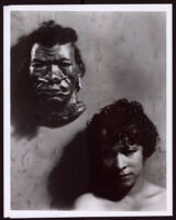 Beulah Woodard standing beside a papier mâché mask of an African man that is mounted on a wall, circa 1937