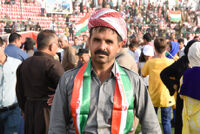 A man wearing Kurdish clothes putting Kurdish flag around his neck