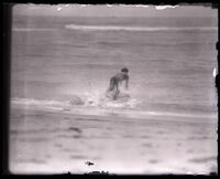 Surfer and Olympic swimmer Duke Kahanamoku in the ocean paddling on a surfboard, Los Angeles, 1920s