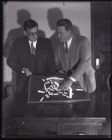 Sheriffs Harry Brewster and F. P. Dickerson looking over a piece of framed broken glass, Los Angeles, circa 1920s