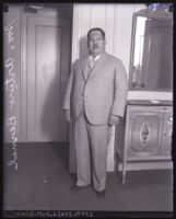 Full length portrait of General Arturo Bernal in suit, standing beside mirror and cabinet, circa 1930