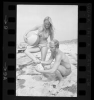 Lifeguard removing oil from feet of woman after Navy oil tanker spill, Doheny State Beach, Calif., 1971