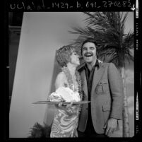 Comedian Carol Burnett posing with Burt Reynolds and his birthday cake, 1972