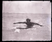 Surfer and Olympic swimmer Duke Kahanamoku on a paddling on a surfboard in the ocean, Los Angeles, 1920s