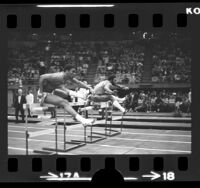 Rod Milburn and another athlete running hurdles at Los Angeles Times Indoor Games, Calif., 1973