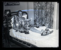 Loretta Turnbull, international outboard motorboat champion, in bed with her trophies, Monrovia, 1931