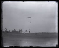 Parachutist Mary Wiggins nearing a ground target above an open field with people watching, Los Angeles, 1931