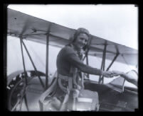 Mary Wiggins, wearing parachute pack and smiling as she climbs onto plane, Los Angeles, 1931