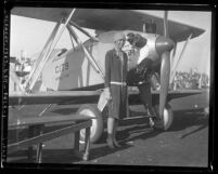 Amelia Earhart wearing a dress standing beside a plane, circa 1928