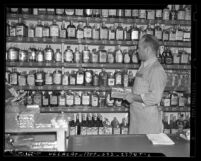 Los Angeles merchant Sam Grossberg updating liquor stamps on bottles for increased tax in 1940