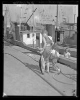 Daughters of fisherman walk down dock with signs on back protesting price cut by canneries on Terminal Island, Calif., 1960