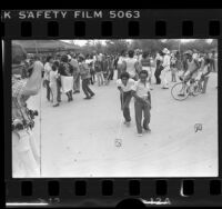Two boys with invisible dog leashes as people dance at Watts Summer Festival, Calif., 1979