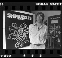 Sam Savage standing before his jigsaw puzzle design named Shmuzzles, 1980