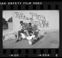 Herman Akins and Steven White sitting under graffiti that helped in investigation of killings in West Los Angeles, Calif., 1980