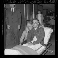 Comedian Peter Sellers sitting up in ambulance gurney with wife Britt Eklund in Los Angeles, Calif., 1964