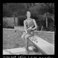 Olympic swimmer Sharon Stouder, sitting on diving board with her medals in Los Angeles, Calif., 1964
