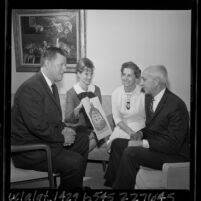 J.D. Morgan and Paul C. Hannum with their wives looking at poster for UCLA Faculty Women's Club dinner, 1965