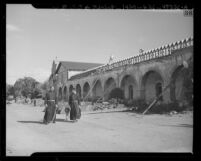 Fathers Kelleher and O'Leary walking through courtyard during restoration of Santa Inés Mission, Solvang, 1947