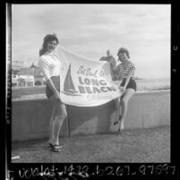 Greeters, Mary Ann McHenry and Darlene Owen on boardwalk, holding up banner reading "Set Sail for Long Beach California", 1956