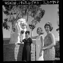 Loyola University of Los Angeles female alumni with school baseball caps standing next to Loyola lion statue, 1965