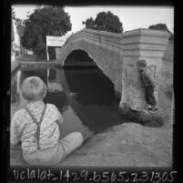 Two boys playing around bridge over canal in Venice, Calif., sign in background reads 