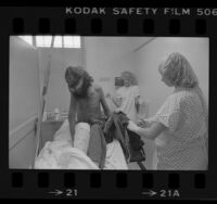 Two nurses cutting clothes off male transient infested with lice at Los Angeles County-USC Hospital, 1985
