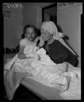 Linda Lee Baker with her grandmother, Sister Ruth Lewis, at Northridge Hospital after the 9-year-old suffered burns from a bombing of the Fountain of the World headquarters, 1958.