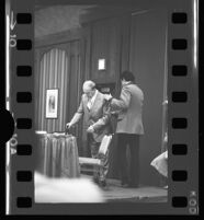 Mickey Cohen is helped into his seat at a question and answer session at the Sheraton Airport Hotel, 1975.