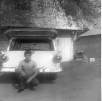 Man crouching in front of car in backyard