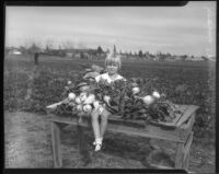 Young girl sits amongst the harvest from a community garden, circa February 1934.