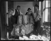 Law enforcement officials George Fisher, Elizabeth Fiske, and J.W. Buckley surrounded by bags of food, Los Angeles, circa 1930