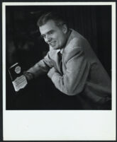 Aldous Huxley seated, smiling and holding a copy of Doors of Perception [descriptive]