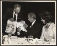 Aldous Huxley looking at cartoons with unidentified man and woman [descriptive]