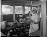 Cook stands with a ladle in the kitchen of a cooperative in Los Angeles, 1930s
