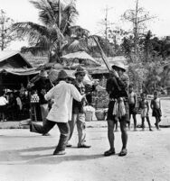 Man playing khaen with umbrella bearer and dancer