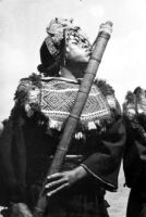 Photo of man in traditional dress playing long bamboo instrument with quill mouthpiece