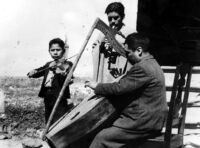 Photo of three men playing; violin, cane flute?, and harp
