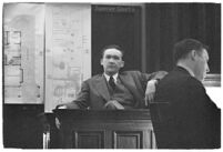Murder suspect Robert S. James sitting on the witness stand with a plan of his house behind him, Los Angeles, 1936