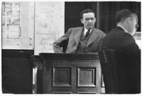 Murder suspect Robert S. James sitting on the witness stand with a map of his house behind him, Los Angeles, 1936