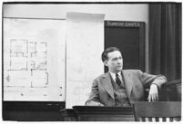 Murder suspect Robert S. James sitting on the witness stand with a map of his house behind him, Los Angeles, 1936