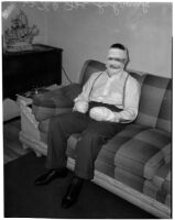 Joe Schrank sits on a couch with his hands and face completely wrapped in bandages, Los Angeles