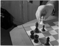 Close-up of a chess board and player's hand moving one of the white bishops, Los Angeles