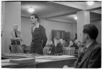 Man testifying (?) during unidentified hearing in courtroom with model cars on table