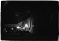 Row of businesses including a liquor store, a cafe, the LA I.D.A. and the Sea Pride Packing Company at night, Los Angeles, 1930s