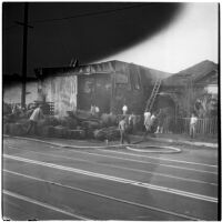 Fire fighters battling a fire in a hay barn while children gather to watch, Los Angeles, 1945